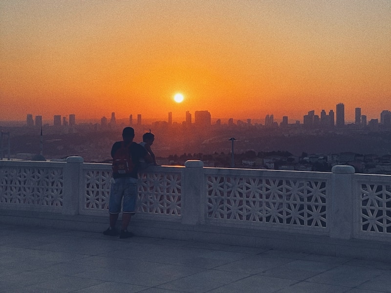 2 women standing on white concrete fence during sunset