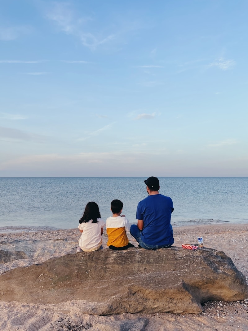 a man and a couple of children sitting on a rock looking at the water